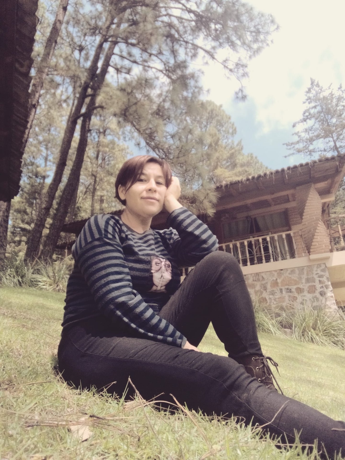 Retrato de Azucena Godínez en bosque, sentada en el pasto con árboles al fondo